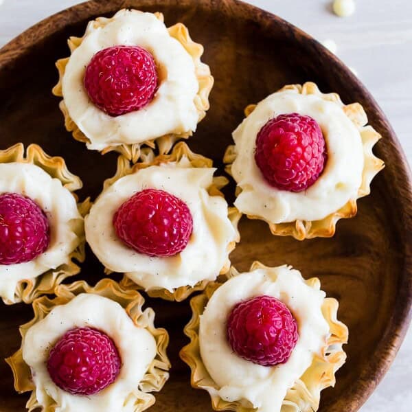 These no bake white chocolate cheesecake phyllo bites are perfectly adorable and topped with fresh raspberries. They are super simple to make and would look perfect on your holiday dessert table.