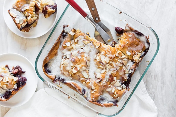 Cherry Fritter Cake in a baking dish on a table with 2 slices of cake on 2 white plates. 