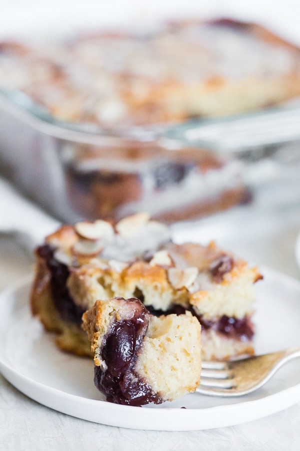 A fork holding a bite of cherry fritter cake. 