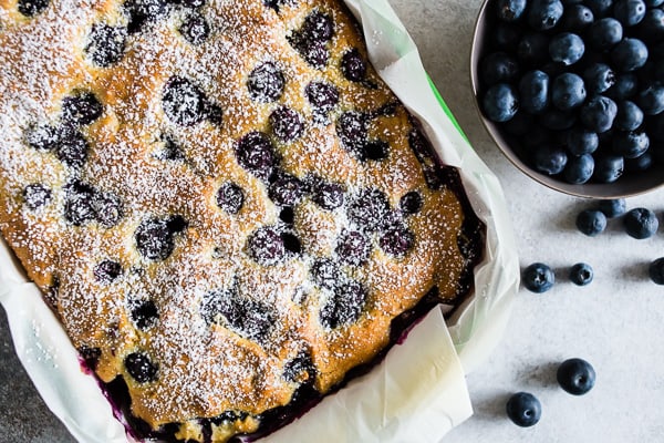 Blueberry Lemon Ricotta Olive Oil Cake sprinkled with powdered sugar and served with extra berries.