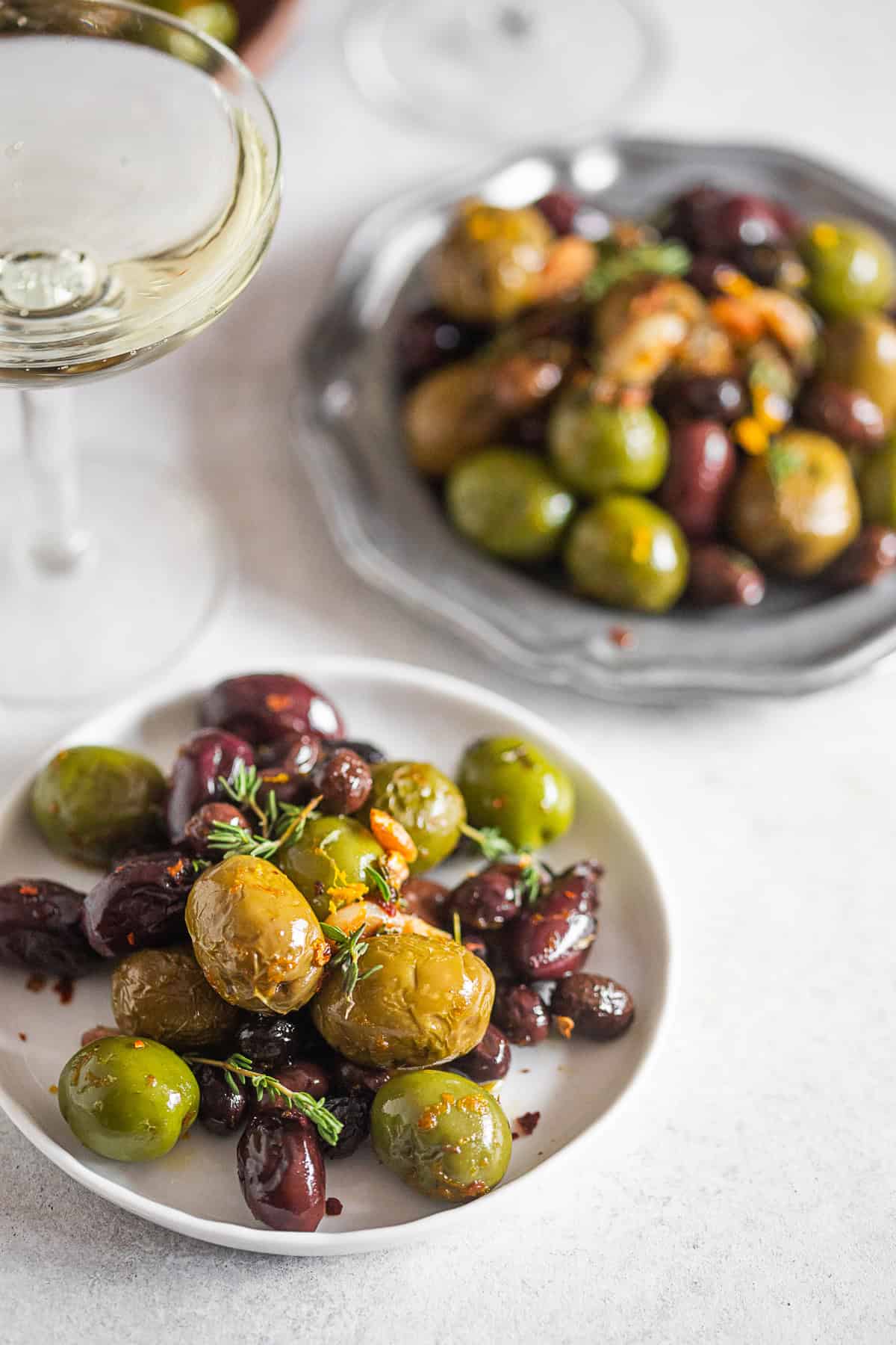 Garlic Herb Roasted Olives on a small white plate with another plate in the back. 