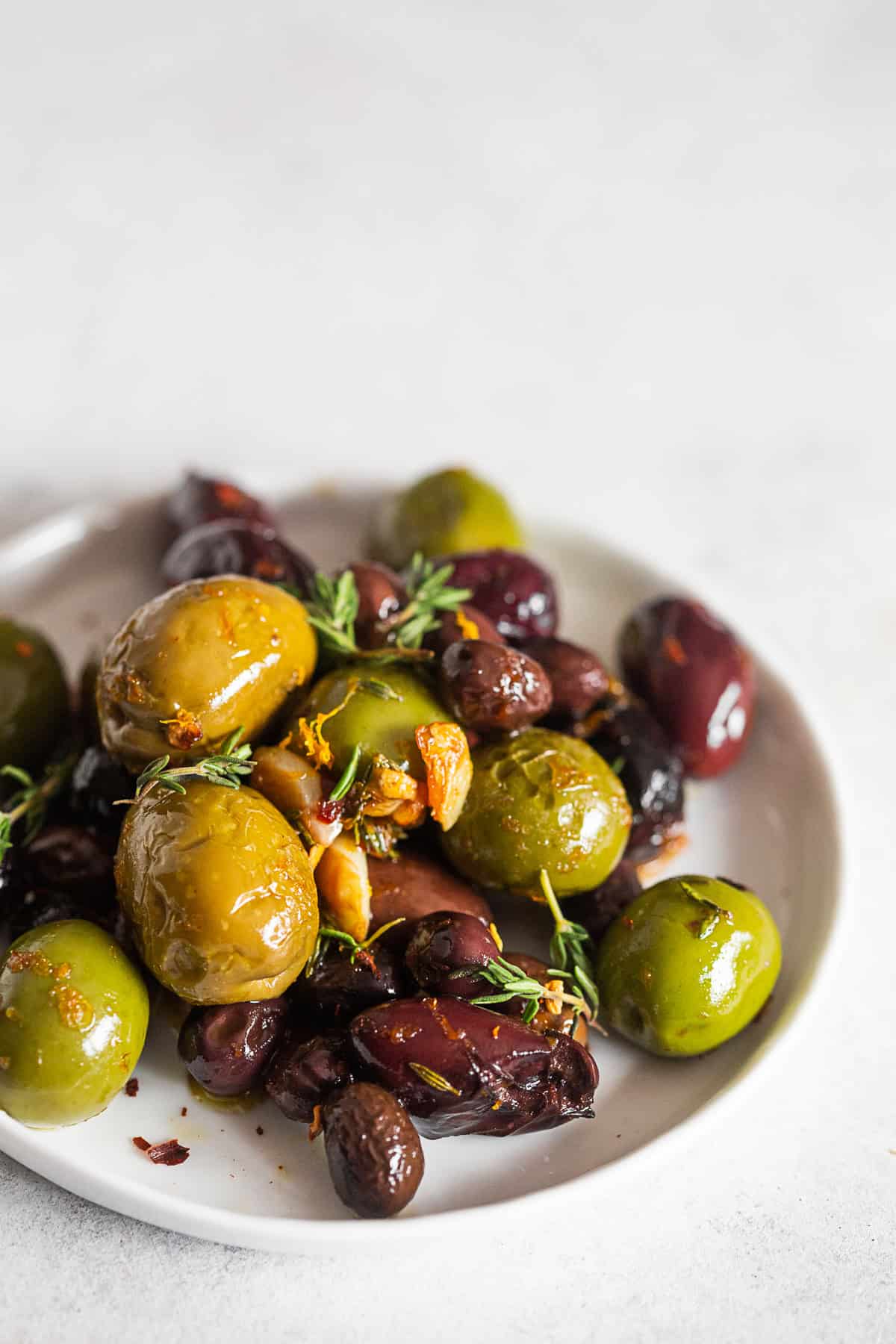 Garlic Herb Roasted Olives on a plate with extra herbs. 