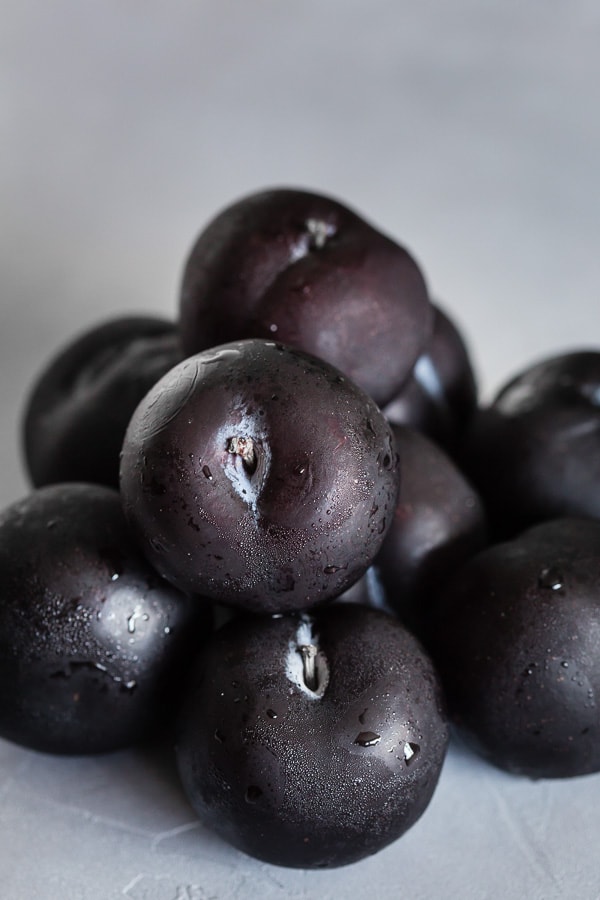 Black plums sitting on a table. 