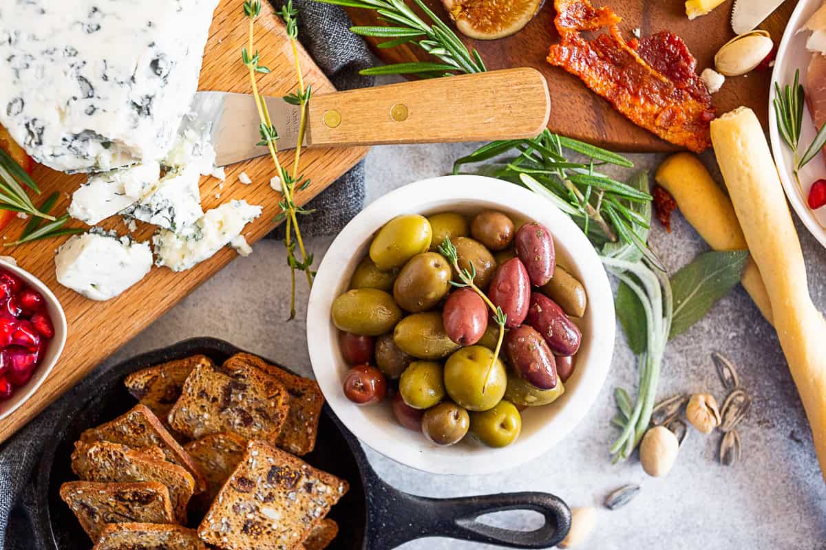 Gorgonzola cheese, seeds cracker, and olives on a table. 