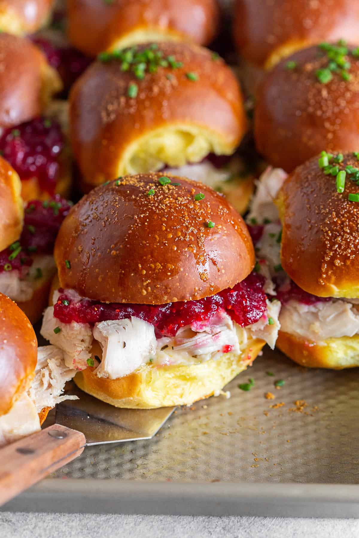 Baked Cranberry Cheddar Turkey Sandwiches on a baking tray with a spatula.