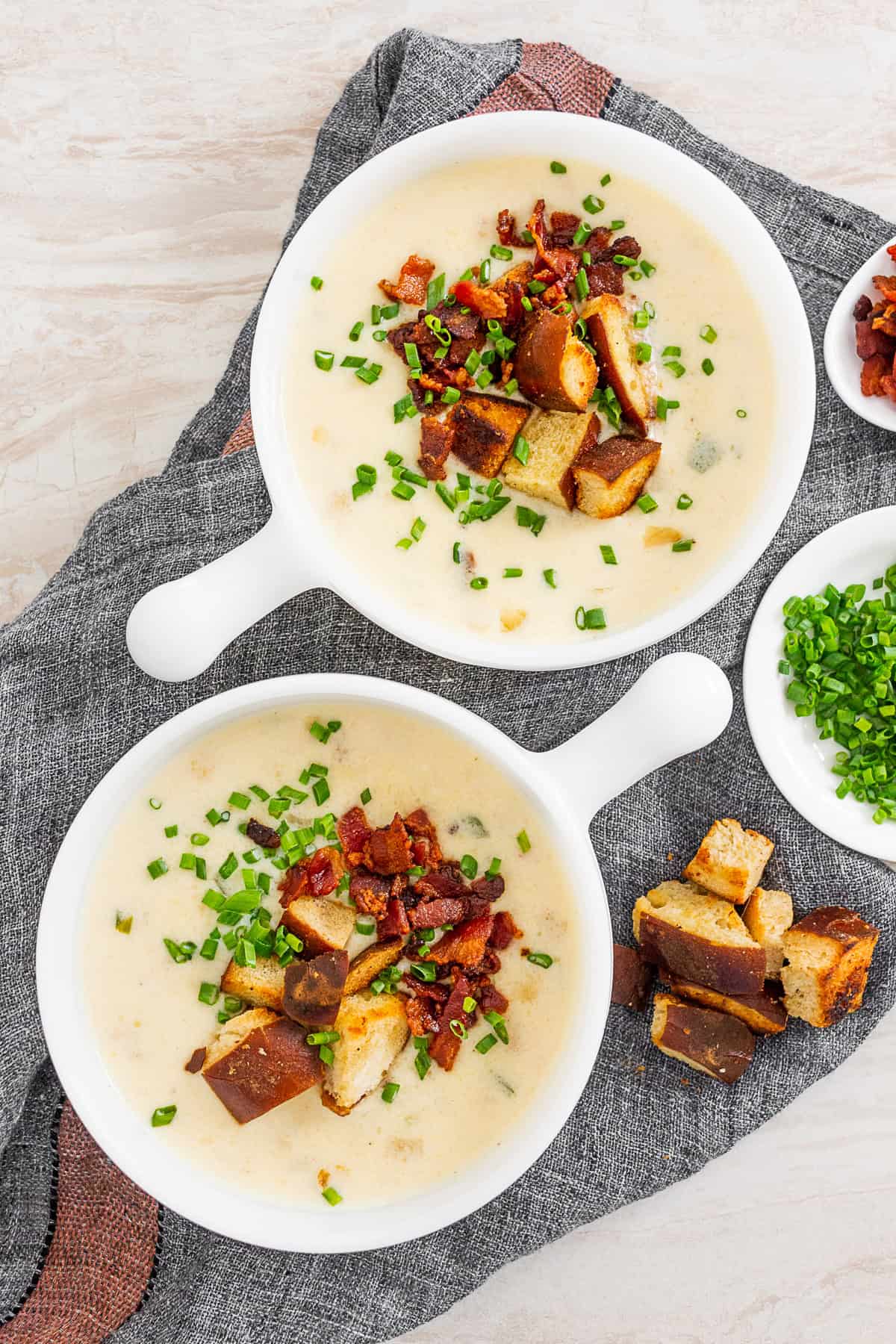 Beer Cheese Soup in 2 white bowls topped with bacon, croutons, and chives. 