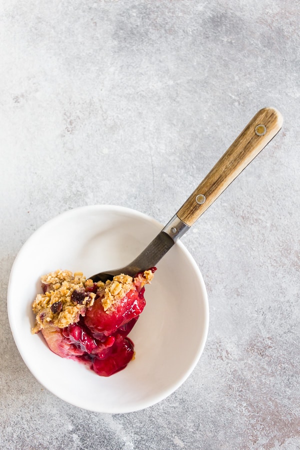Cardamom Vanilla Plum Crisp spooned into a small white bowl. 