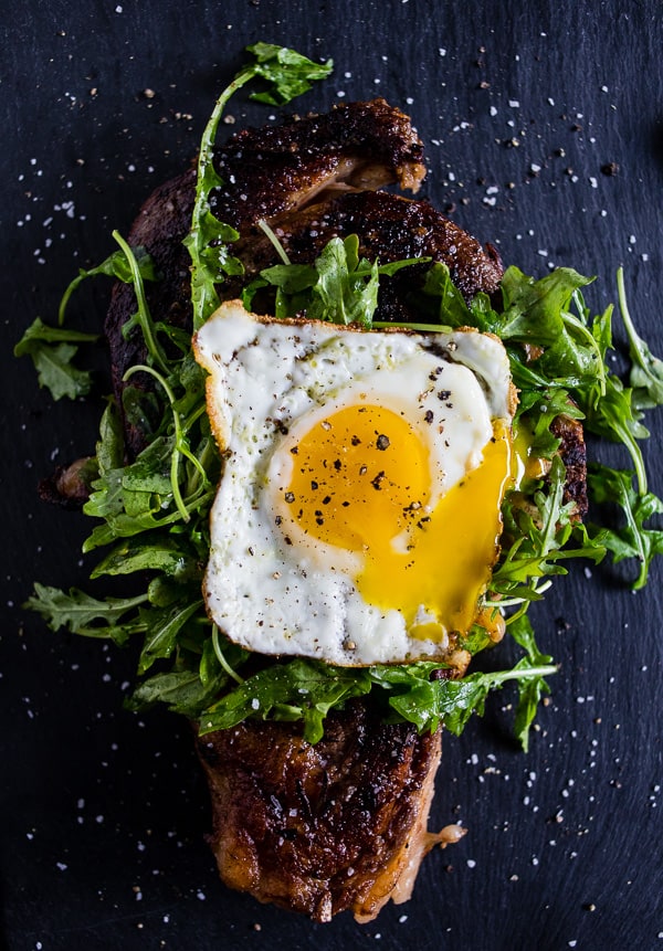 fried egg topped grilled steak with arugula leaves under the egg