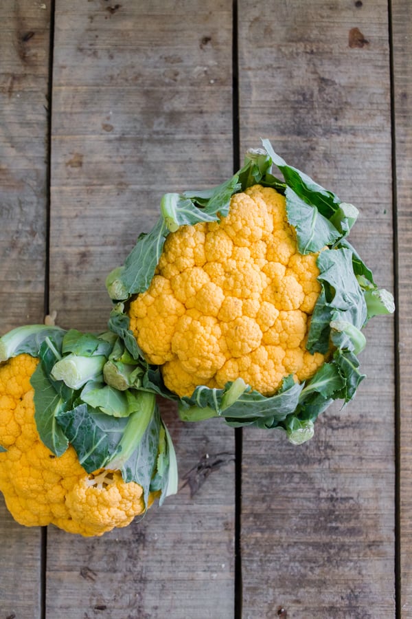 2 heads of orange cauliflower on a wooden table.