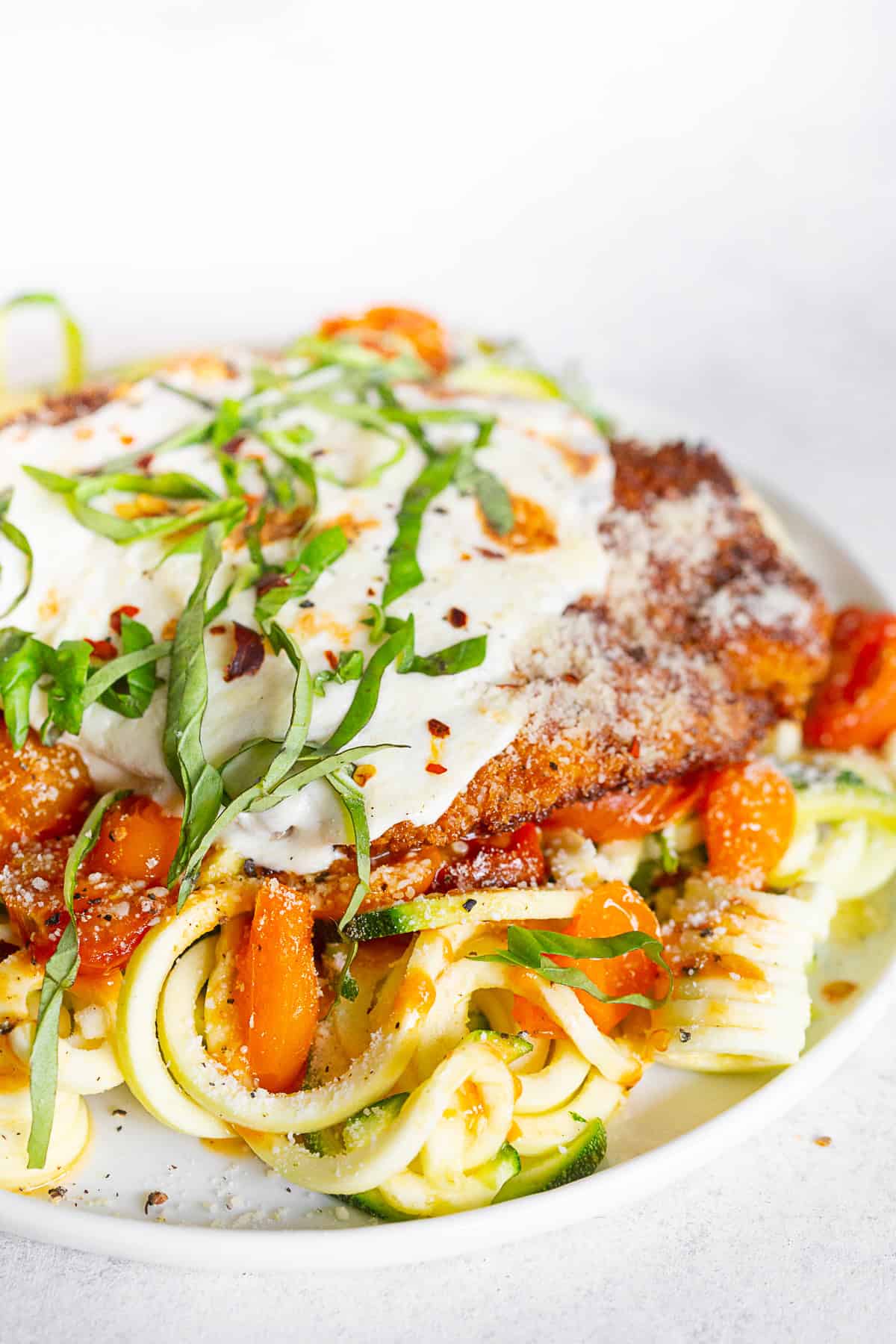 Summer chicken parmesan served over a pile of zoodles.