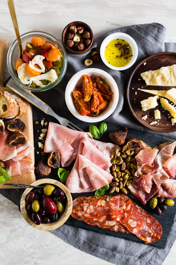 Meats, olives, cheese, nuts and bread on a board and in bowls.