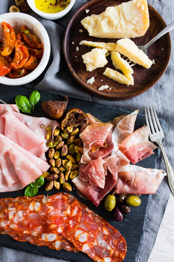 Cured meats, nuts, roasted tomatoes, and cheese on a board.