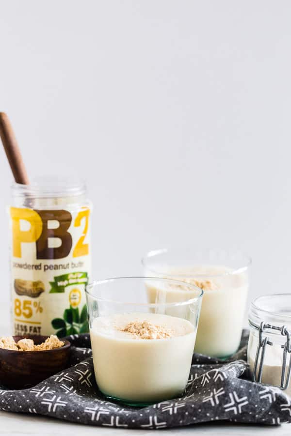 Two glasses of peanut butter smoothie with jar of PB2 powder in the backround.