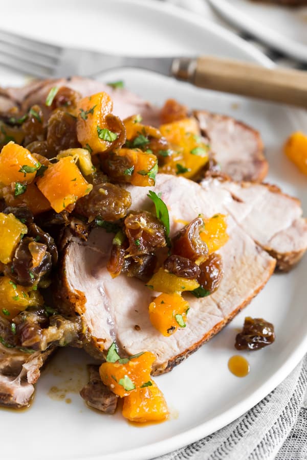This roast pork loin with dried fruit compote is an easy and flavorful dinner recipe that your whole family will love. Serve with rice, buttered noodles or even mashed potatoes. Juicy roast pork served with a homemade compote made out of golden raisins, dried apricots, dates, orange juice and just a touch of cilantro. So good! Roast Pork Loin with Dried Fruit Compote on a plate.