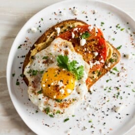This shakshuka hummus toast is a healthy and flavorful way to start the day. Middle eastern spiced roasted tomatoes served on top of hummus toast with a runny egg, fresh herbs, and salty feta cheese.