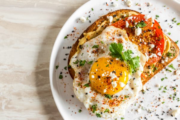 Shakshuka Hummus Toast on a plate topped with sesame seeds and a fried egg.