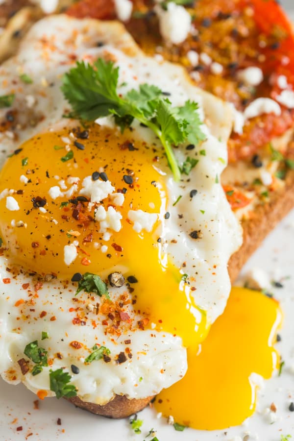 Shakshuka Hummus Toast topped with a runny fried egg.
