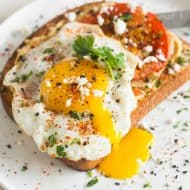 This shakshuka hummus toast is a healthy and hearty breakfast. Hummus spread toast topped with spiced roasted tomatoes, fried egg, cilantro and feta cheese.