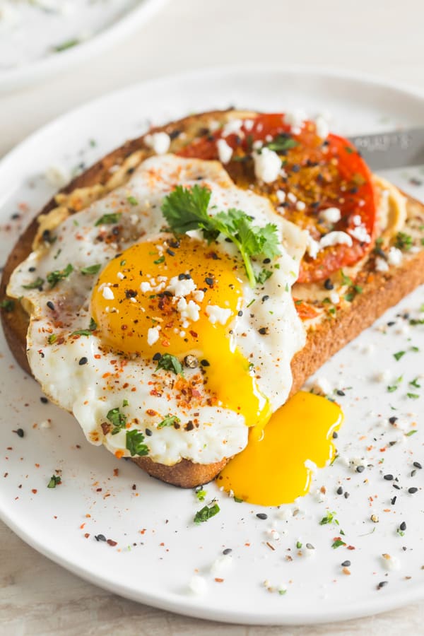 Shakshuka Hummus Toast topped with an egg, feta, and sesame seeds.
