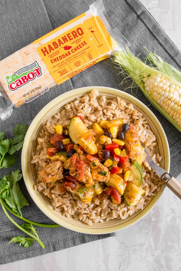 tex mex chicken and vegetable skillet on a plate with rice and wedge of cheese.