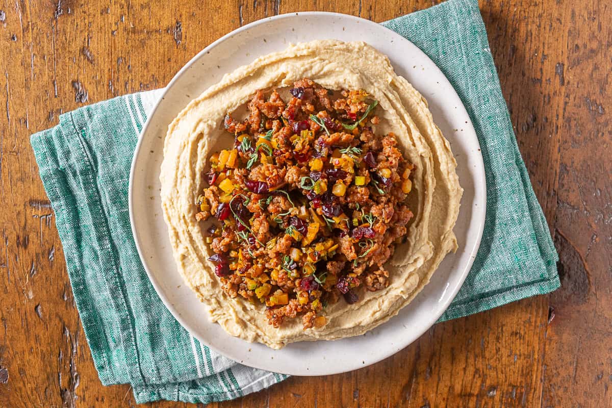 thanksgiving stuffing topped hummus on a white plate with a green napkin underneath