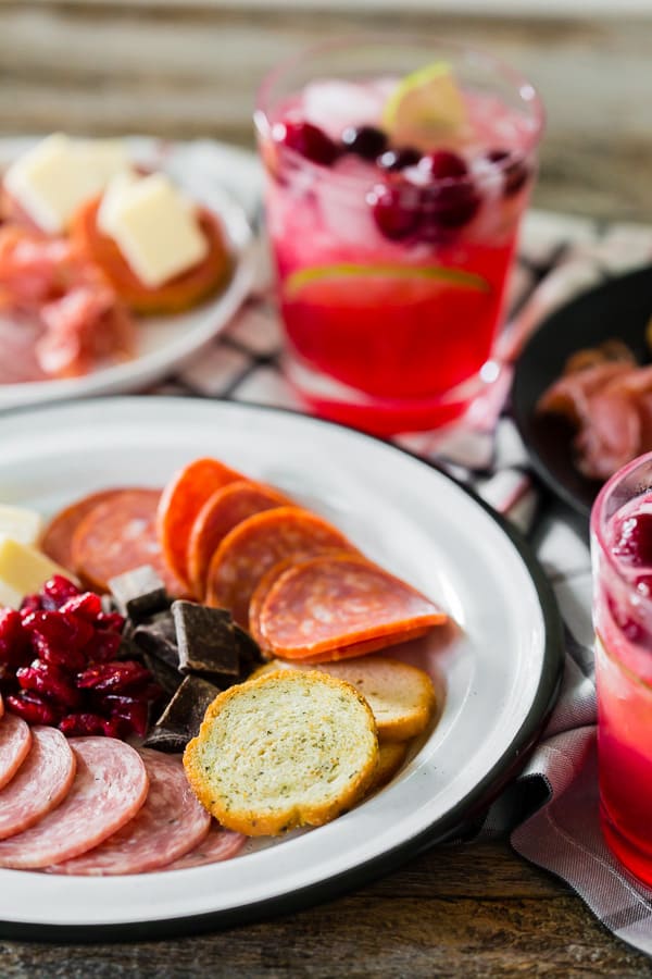 close up shot of meat and cheese on a plate with a cranberry lemonade ginger beer cocktail in the background