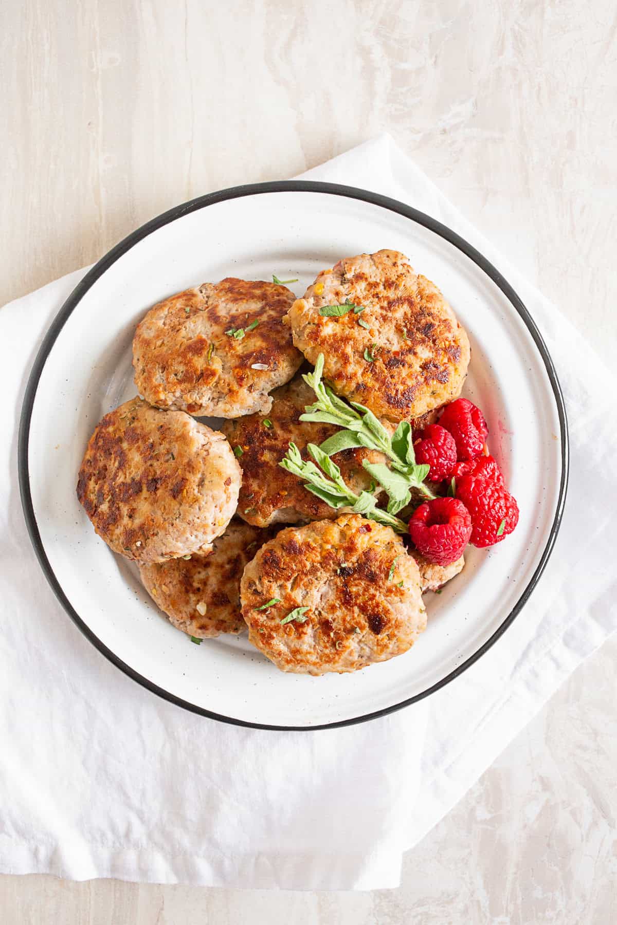 Homemade Chicken Sausage Patties on a plate with fresh herbs and berries. 