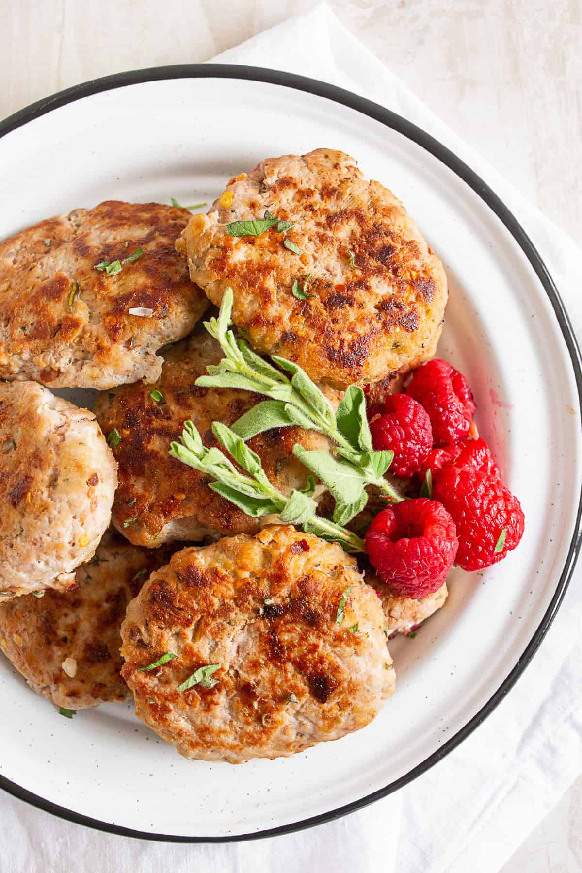 Chicken sausage patties on a plate with fresh berries and herbs. 