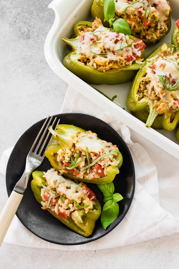 ground chicken stuffed bell peppers cut in half on a black plate with full peppers in the background