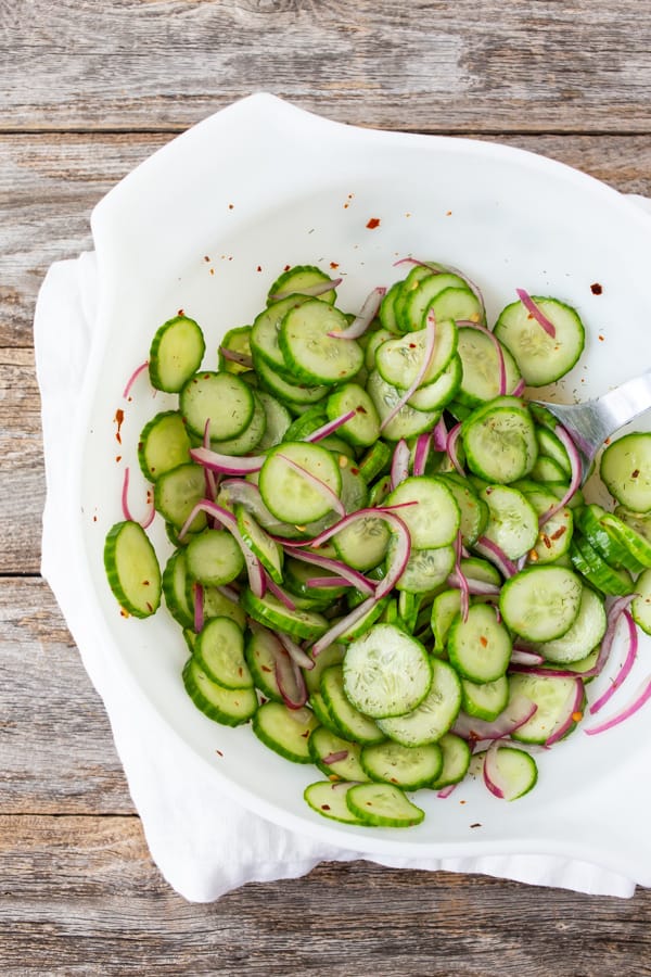 sliced cucumber salad with sliced red onion in a white bowl.