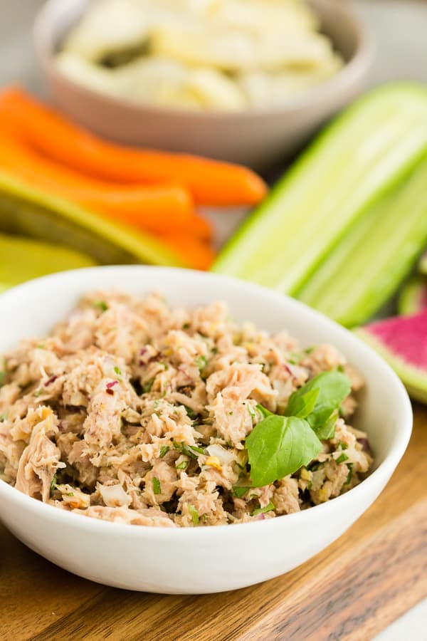 lemon herb tuna salad in a small white bowl with veggies in the background