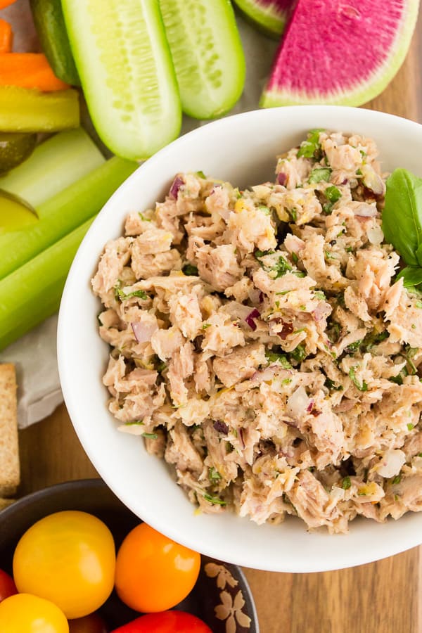 lemon herb tuna salad in a white bowl surrounded by cracker and vegetables