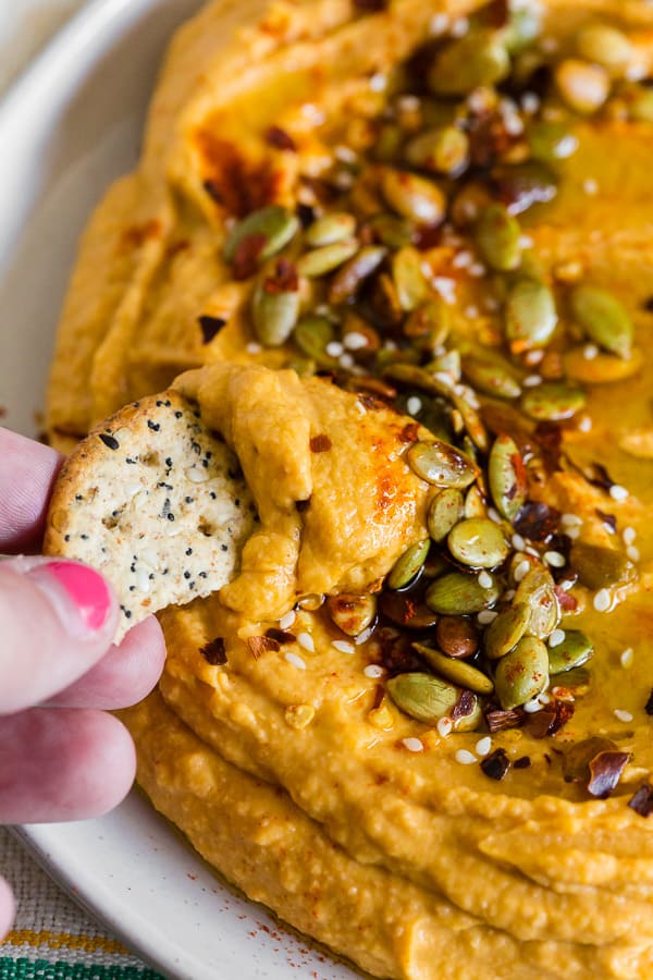 close up of a cracker being dipped into pumpkin hummus.