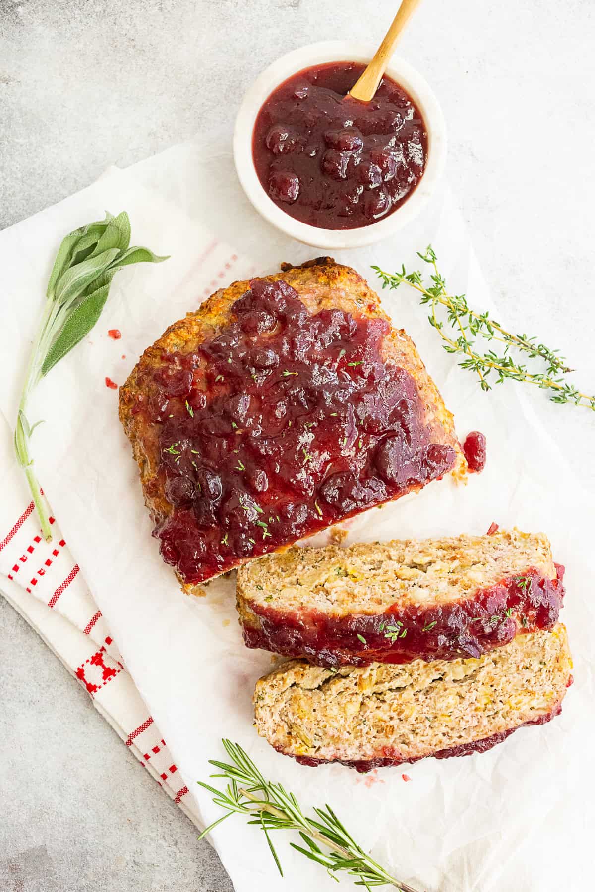 Thanksgiving turkey meatloaf sliced and staged with fresh herbs and extra cranberry sauce.