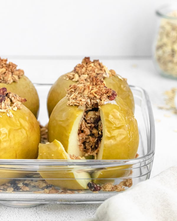 oatmeal stuffed breakfast baked apples sitting in a dish with a slice cut out to show the center. 
