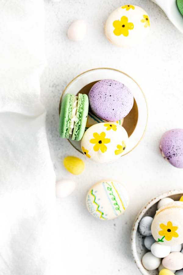 Easter egg macarons in a bowl decorated with flowers and speckled paint