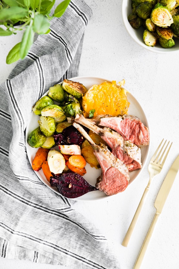 a plate with lamb chops, roasted vegetables, brussels sprouts, and scalloped potatoes.