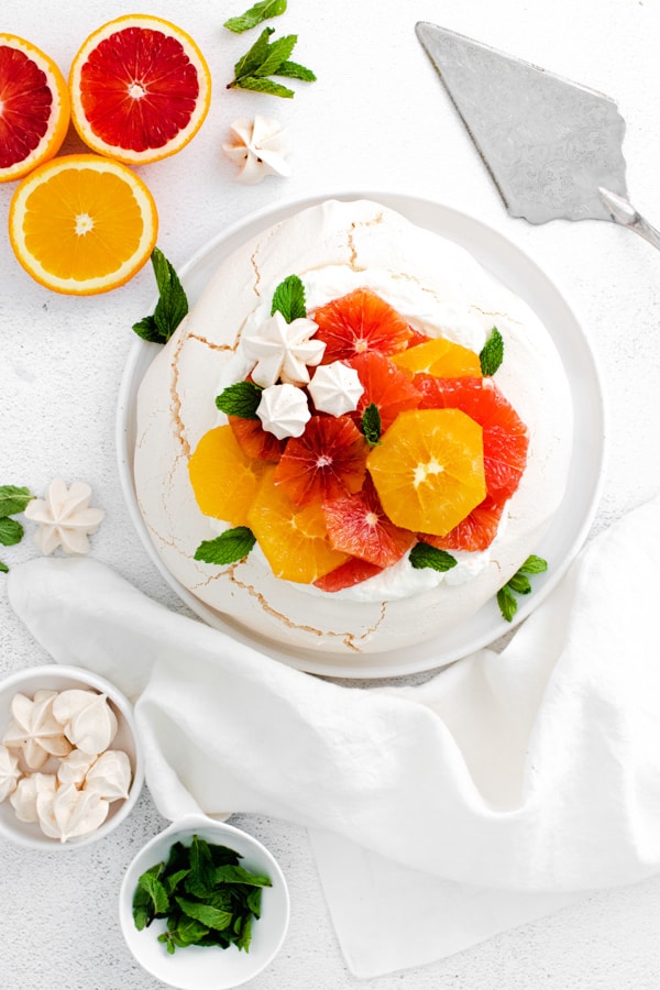 winter citrus pavlova sitting on a plate with a cake server.