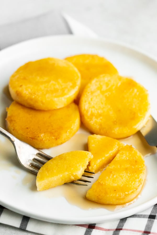 fried cornmeal mush on a white plate with maple syrup and a fork. 