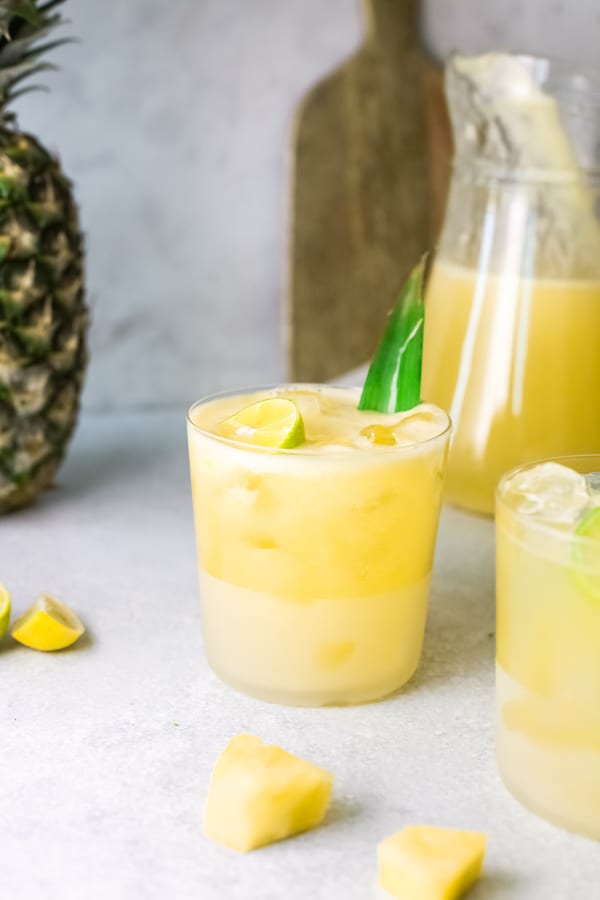 Pineapple Agua Fresca in a glass with a pitcher in the background.