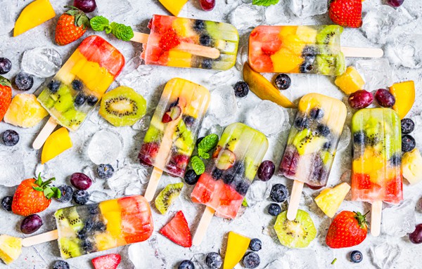 rainbow fruit popsicle on a serving tray with ice and lots of fresh fruit.