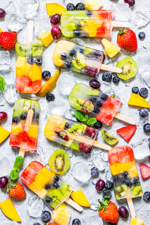 Rainbow Fruit Popsicles on a serving board with ice and fresh fruit.