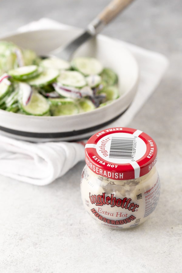 a jar of horseradish sauce sitting in front of a bowl of creamy horseradish cucumber salad.