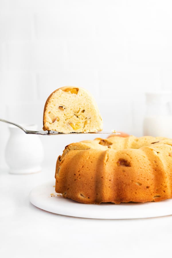 Peach Bundt Cake with a sliced being lifted out of the cake. 