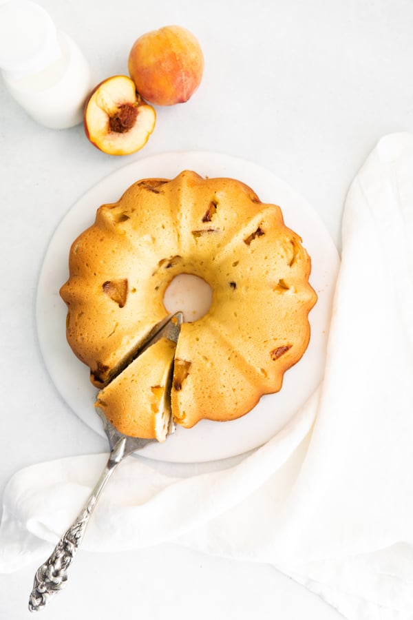 Peach Bundt Cake on a serving platter with a sliced pieces on a server knife. 