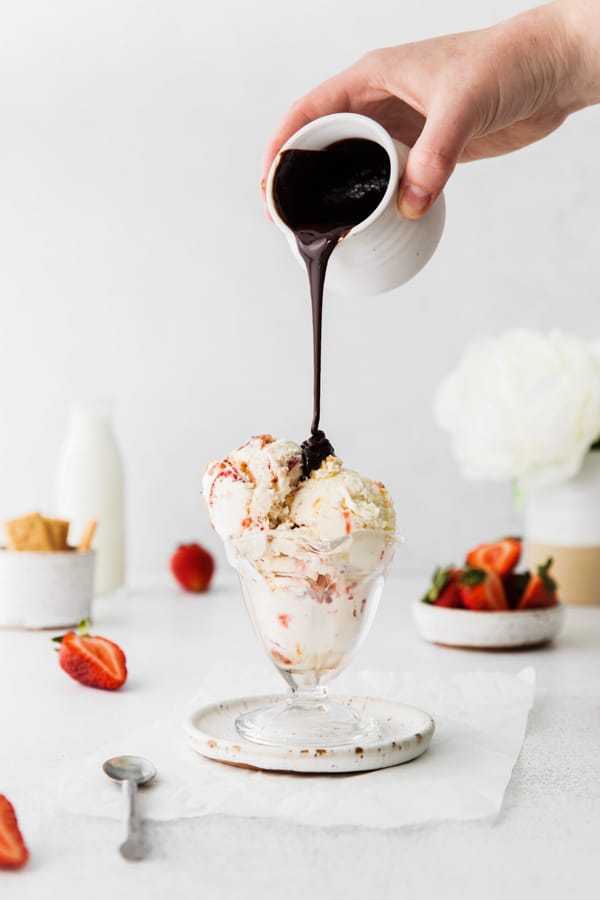 chocolate sauce being poured over strawberry cheesecake ice cream.