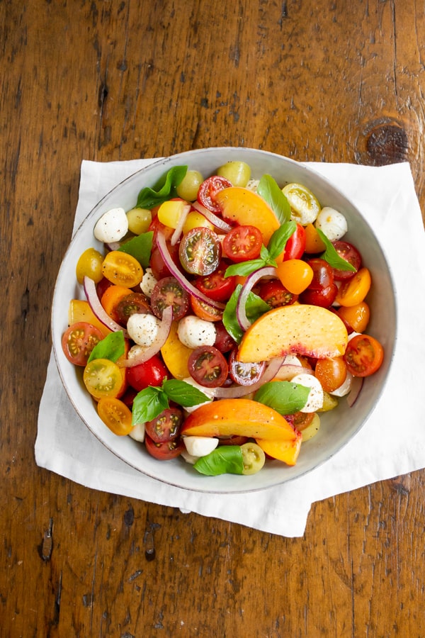 Tomato Peach Caprese Salad in a bowl sitting on a white napkin.