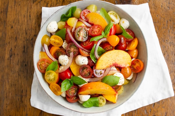Tomato Peach Caprese Salad in a bowl sitting on a wood table.