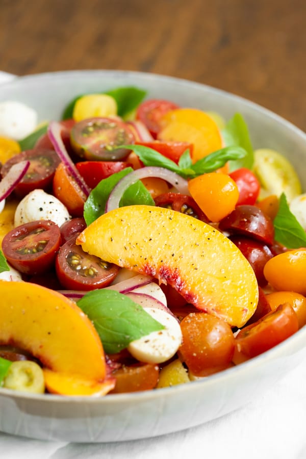 Tomato Peach Caprese Salad in a bowl with fresh basil.