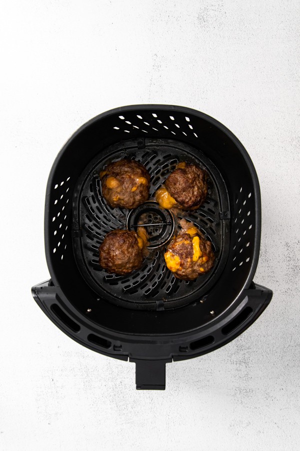 4 air fryer Juicy Lucy burger sitting in the air fryer basket. 